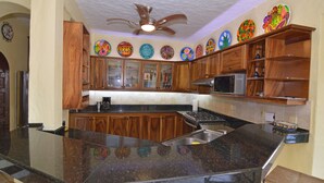 Cozinha com armários de madeira, bancada de granito, ventilador de teto e pratos decorativos na parede.