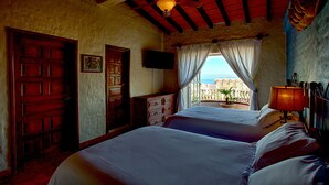 Quarto com duas camas, porta de madeira, televisão e vista para o mar.