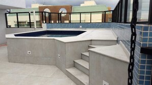 Une piscine sur le toit, dont le bord est recouvert de carreaux bleus, entourée d’une terrasse en béton et accessible par des marches.