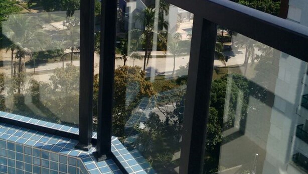 Un balcon doté d’une balustrade en verre, offrant une vue sur le paysage urbain et les montagnes qui se dessinent à l’horizon.