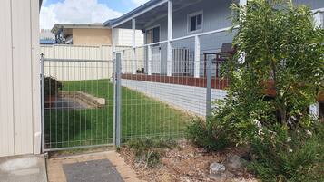 A fenced backyard with a small lawn, a wooden deck, and a metal gate.