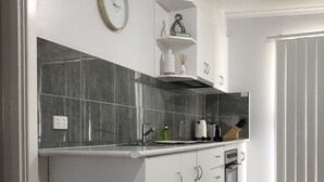 A modern kitchen with white cabinets, a built-in oven, and a coffee maker. There is a small shelf with a "Welcome" sign and a bottle of hand soap.