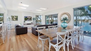 A spacious living area with a wooden dining table, white chairs, and a grey sofa. - Magical Water Views for the whole family (Gold Coast)