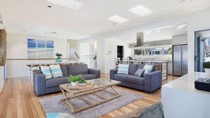 A modern living room with two sofas, a glass coffee table, and a kitchen in the background. - Magical Water Views for the whole family (Gold Coast)