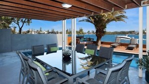 A covered outdoor dining area with a pool, chairs, and a table. - Magical Water Views for the whole family (Gold Coast)