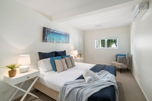 A bedroom with a bed, bedside tables, a chair, a window, and a painting on the wall.