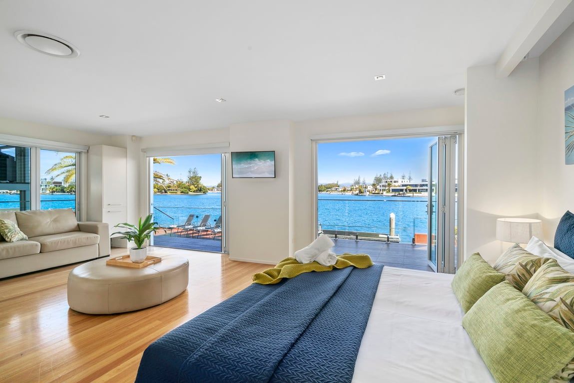 A modern hotel room with a large bed, a sofa, and a view of a body of water through large windows.