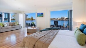 A modern hotel room with a large bed, a sofa, a round ottoman, and a balcony with a view of the sea. - Magical Water Views for the whole family (Gold Coast)