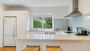 Una cocina moderna con una isla central, armarios blancos, lavavajillas integrado y una ventana con vistas a zonas verdes.