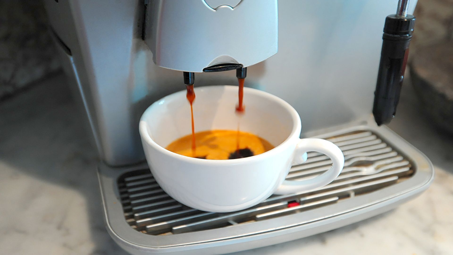 Una máquina de café sirviendo espresso en una taza blanca.