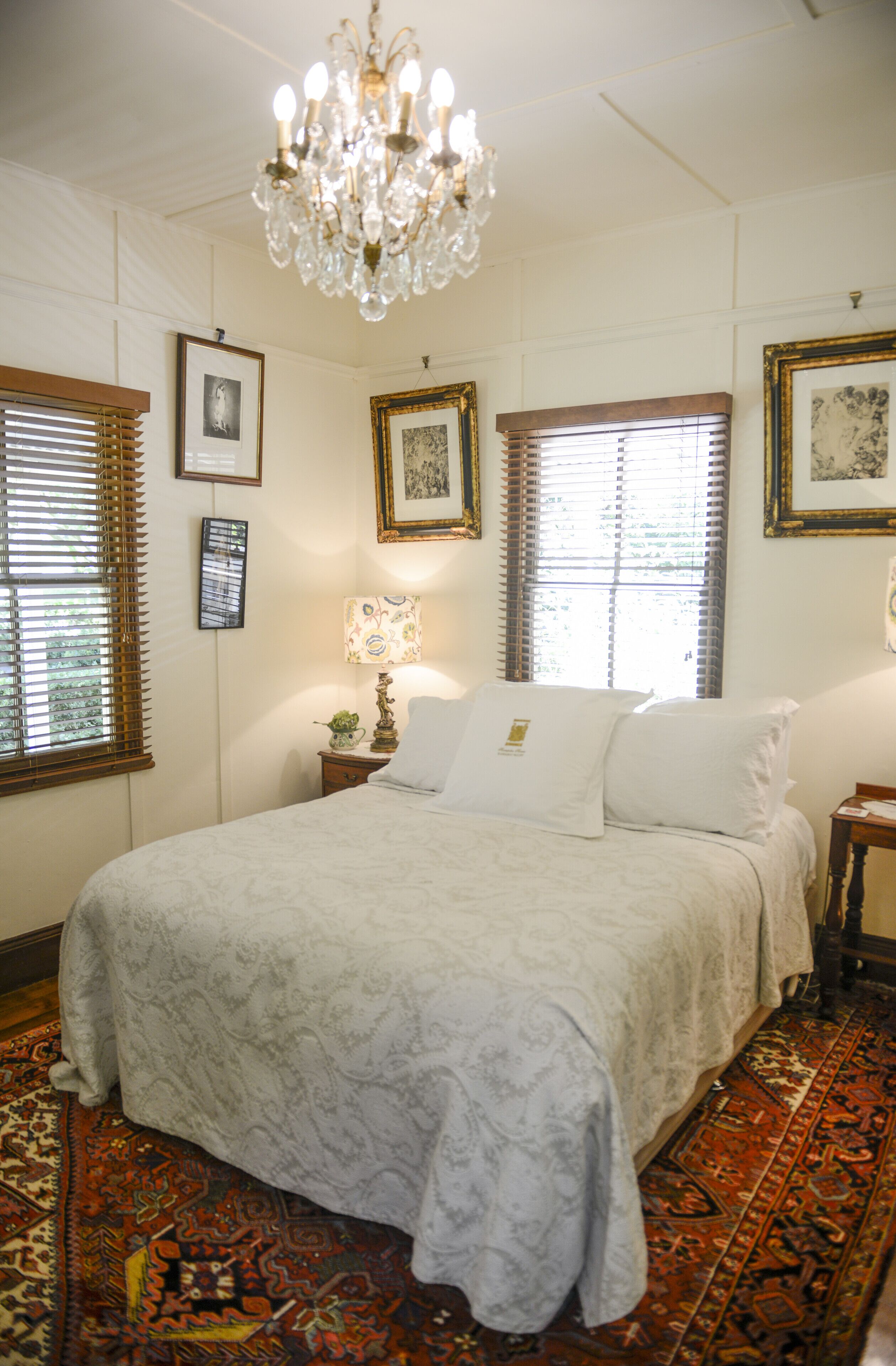 Quarto com uma cama grande, um candelabro, quadros nas paredes e um tapete estampado.