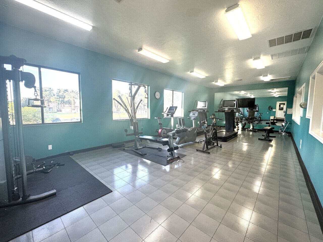 A gym with exercise equipment, large windows, and a tiled floor.