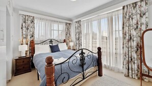 Ein Schlafzimmer mit einem Bett, Nachttischen, einem Sessel und Vorhängen.