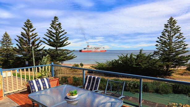 Ein Deck mit Tisch und Stühlen, mit Blick auf ein Gewässer, in der Ferne das Schiff "The New Spirit of Tasmania".