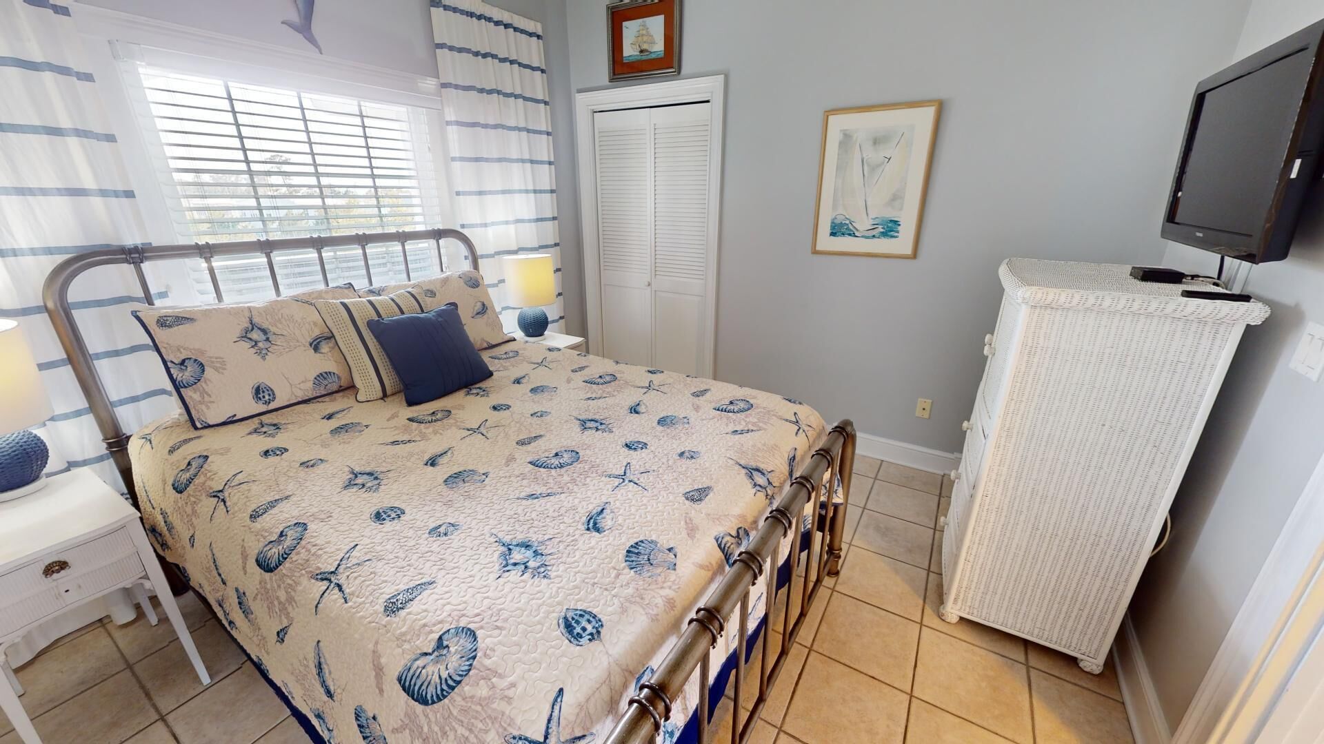 A bedroom with a bed, a bedside table, a nightstand, a wardrobe, a television, and a window with blinds.