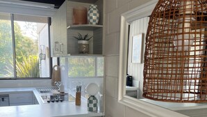 Eine moderne Küche mit großem Fenster, weißen Schränken und einem Essbereich mit weißem Tisch und Stühlen.