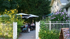 An outdoor seating area with tables and chairs, surrounded by a white picket fence and lush greenery.