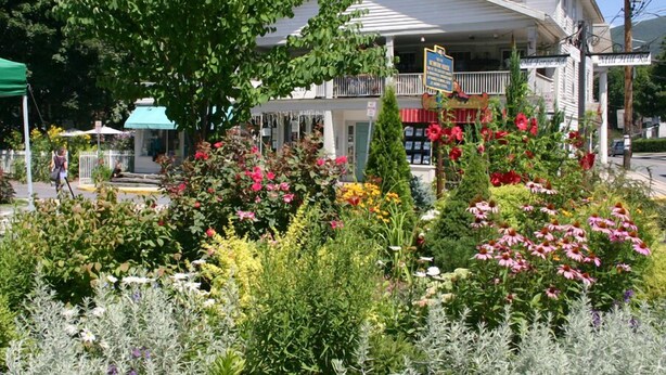 A two-story building with a balcony, surrounded by a variety of colorful flowers and plants.