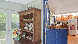 A kitchen with wooden cabinets, a blue door, and a window overlooking a garden.