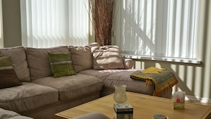 A living room with a beige sofa, a wooden coffee table, and a window with blinds.