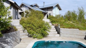 A modern house with a swimming pool, wooden deck, and a staircase leading to the entrance.