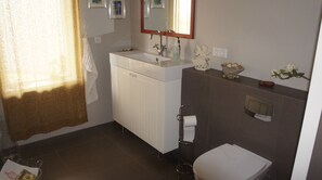 Une salle de bain avec un lavabo blanc, un miroir, des toilettes et un espace douche.
