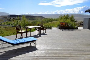 Une terrasse en bois avec un fauteuil de relaxation, une table et deux chaises.