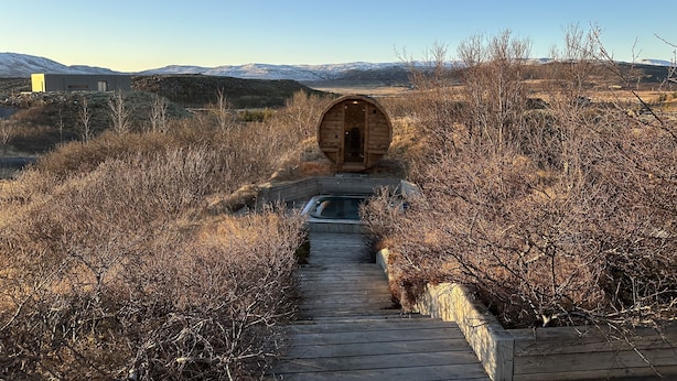 A wooden cabin with a circular entrance, surrounded by dry bushes and a clear sky.