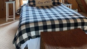 Une chambre mansardée chaleureuse, avec une couvre-lit à carreaux, une décoration murale représentant une tête de cerf et un coussin invitant à la détente.