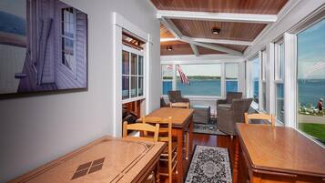 A sunroom with a view of the sea, wooden furniture, and a large painting on the wall.
