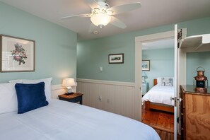 A bedroom with a bed, a nightstand, a ceiling fan, a lamp, and a wooden dresser.