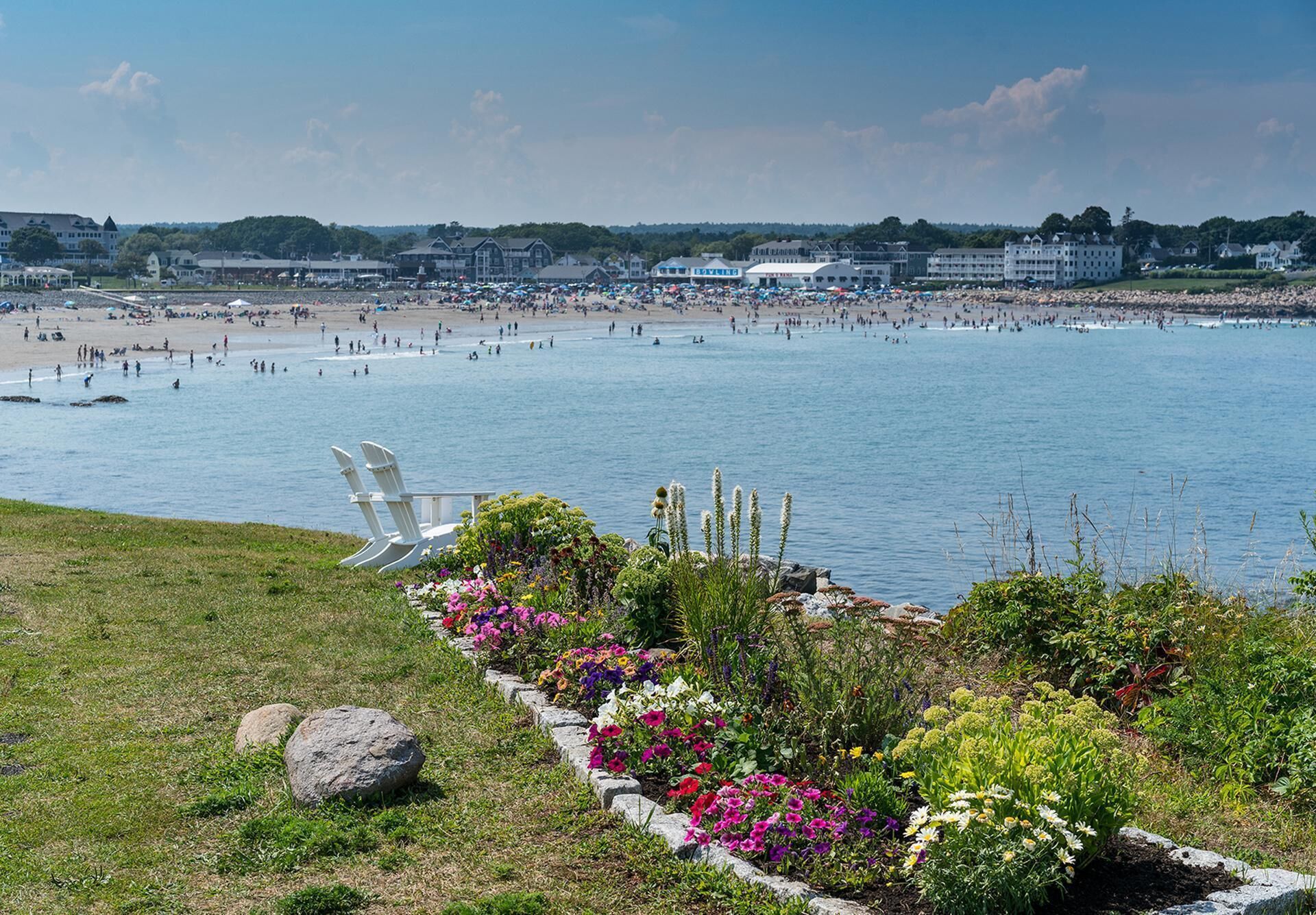A beach with a chair and flowers in the foreground, and a large building in the background.