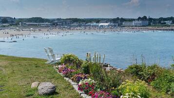 A beach with a chair and flowers in the foreground, and a large building in the background.