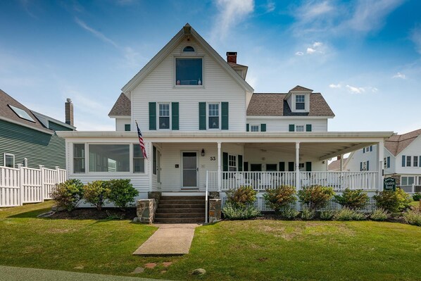A two-story house with a front porch, a flag, and a number "53" on the door.