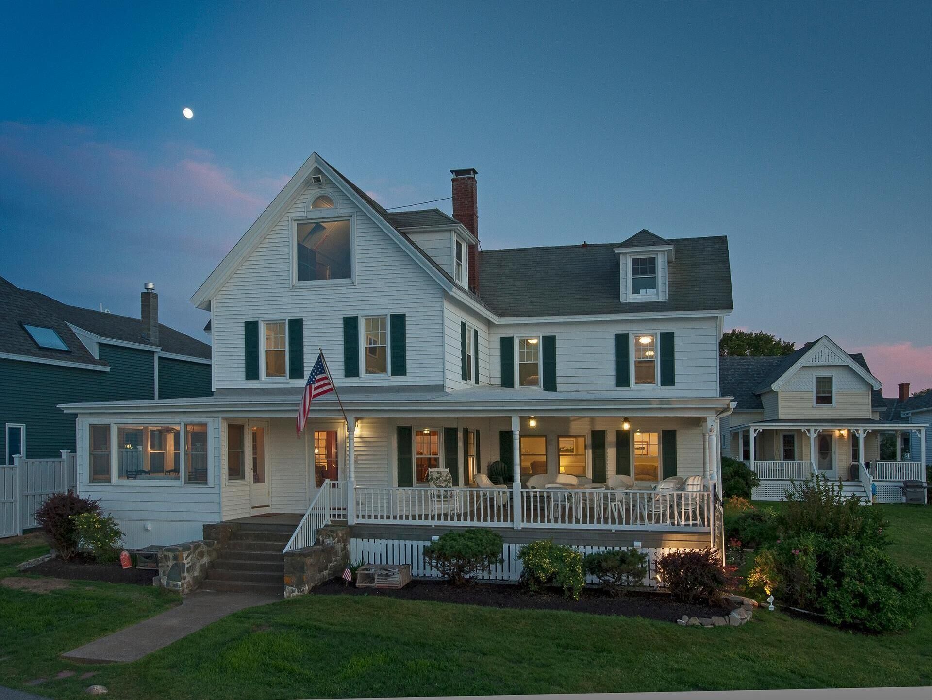 A two-story house with a porch, a flag, and a well-maintained lawn.