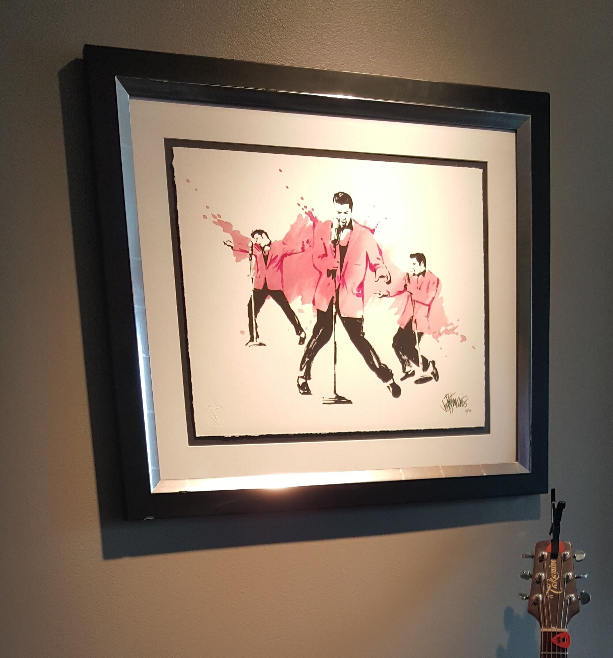 A framed artwork depicting three figures in pink jackets, signed by the artist.