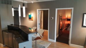 Une cuisine moderne avec un plan de travail foncé, des luminaires suspendus et un coin repas avec une chaise.