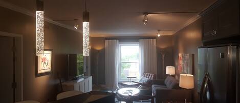 A modern kitchen with a dining area, featuring pendant lights, a refrigerator, and a view of the outdoors.