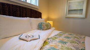 A neatly made bed with a floral-patterned bedspread, a pillow with a leaf design, and a framed picture on the wall.