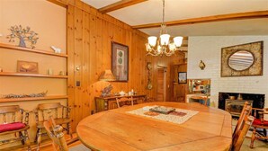 A wooden-paneled room with a round wooden table, chairs, a chandelier, and a fireplace. - Location! Walk to Cranmore and Town! (Conway)