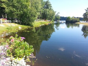 A calm lake with a white fence and lush greenery. - Beautiful Log Home in Suissevale on Lake Winnipesaukee with Beach Access (Moultonborough)