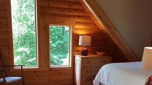 Una camera da letto mansardata accogliente con pareti in legno, una grande finestra, un letto, un comò e un tappeto in pelle di bovino.