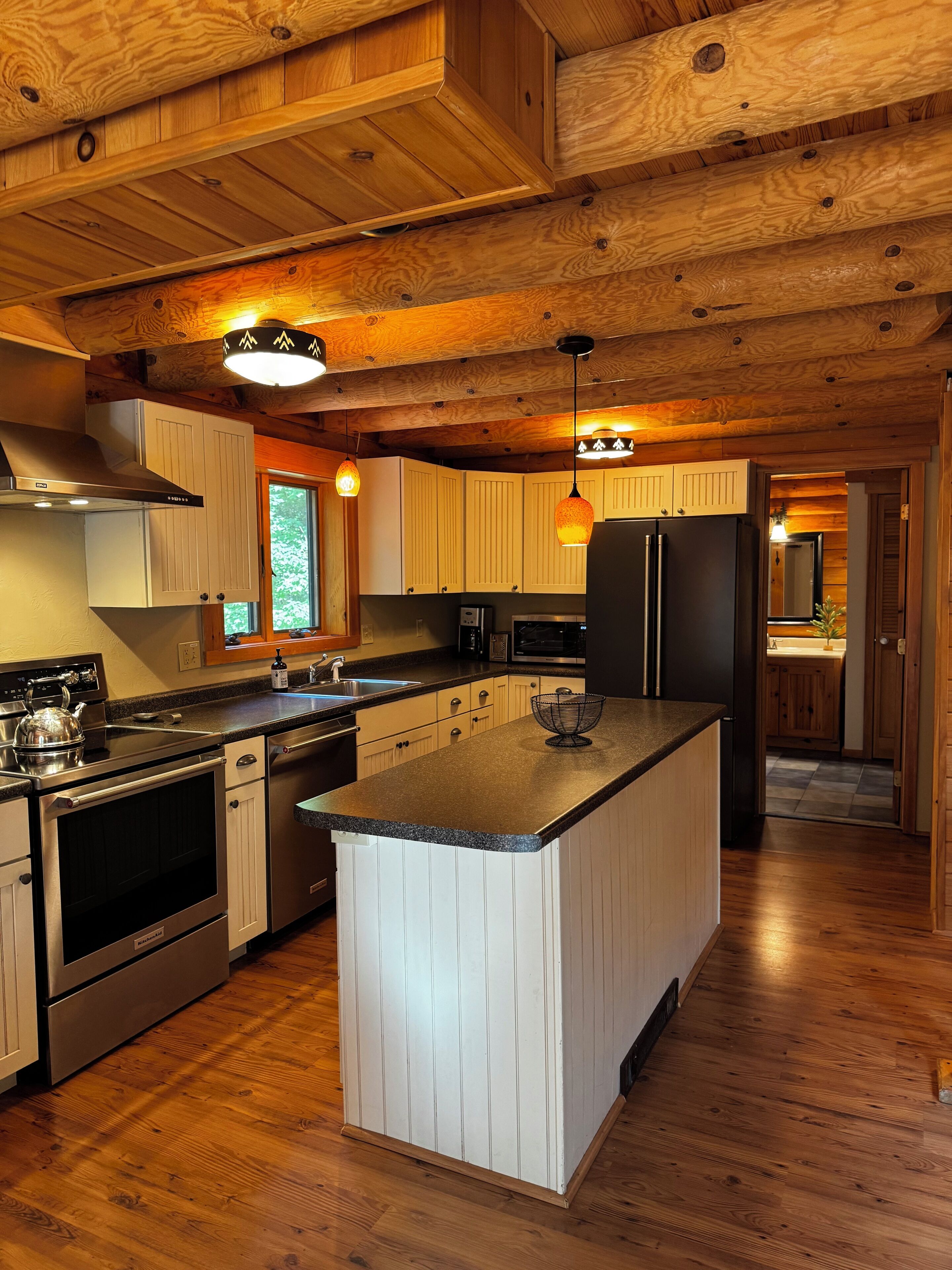 A kitchen with wooden cabinets, a central island, stainless steel appliances, and pendant lighting.