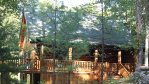 Una baita con un patio in legno, circondata da alberi e rocce.