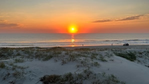 Uma praia com dunas de areia e um pôr do sol sobre o oceano.