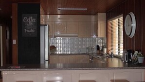 A kitchen with wooden cabinets, a central island with stools, a chalkboard with 'Coffee is Possible', and a clock on the wall. - The Winerack- spectacular views (Mudgee)
