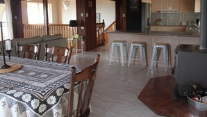 A cozy dining area with a patterned tablecloth, wooden chairs, and a bench. A kitchen with a coffee station and stools is visible in the background. - The Winerack- spectacular views (Mudgee)