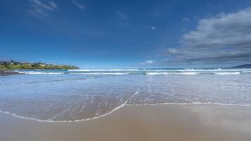 A beach with waves, a clear sky, and buildings in the background.