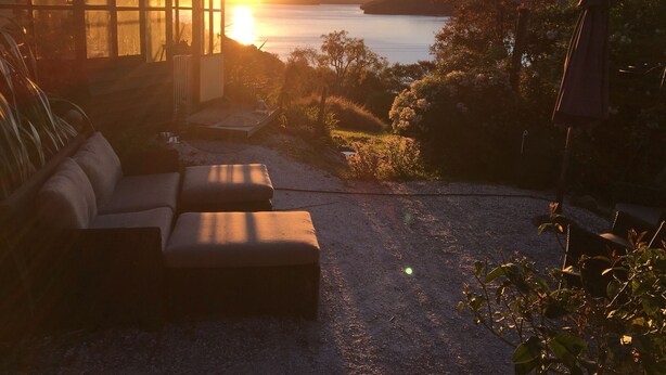 A cozy outdoor seating area with a sofa and ottoman, overlooking a lake and hills at sunset.