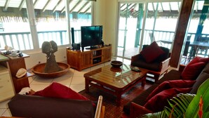 Una sala de estar con televisor, muebles de madera y un ventanal con vistas a una terraza de madera.